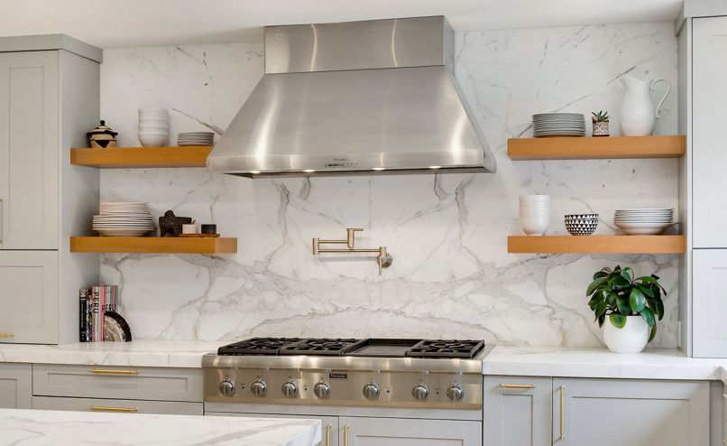 Homeowner and designer Molly Brown demolished her existing kitchen, and in its place installed a workable space in a transitional style that better suited family life. The improvements included Thermador appliances and Bellmont cabinets, which are topped by counters and backsplashes of Calcutta marble. White oak accents such as the open shelves from Stusser Woodworks near the stovetop and the flooring from Pravada provide warmth and textural interest.