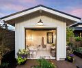 Designed as a she shed with glass garage door, the space opens onto raised beds and BBQ to further the garden party theme. Northwest Finishes hand stenciled floor. White-painted James Hardie board and batten exterior plays off shiplap Hardie siding on residence. Classic Home Element Club chair, Bassett Riley Cube Ottoman, and Noir Wine Table from KEY Home furnishings.