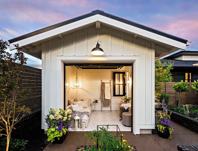 Designed as a she shed with glass garage door, the space opens onto raised beds and BBQ to further the garden party theme. Northwest Finishes hand stenciled floor. White-painted James Hardie board and batten exterior plays off shiplap Hardie siding on residence. Classic Home Element Club chair, Bassett Riley Cube Ottoman, and Noir Wine Table from KEY Home furnishings.