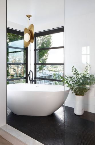 A long shower room in the master bath is anchored at one end by a white, freestanding soaker tub from which bathers can enjoy views of Lake Union. Black penny marble tiles cover the floor and the brass light fixture is approved for a damp location.