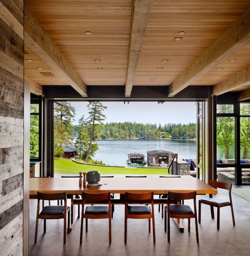 The new home, built to fit the vernacular of the historic compound, is situated on a knoll above great lawn looking toward Salish Sea through Quantum aluminum clad lift and slide doors. Custom dining table with stackable DWR profile chairs.