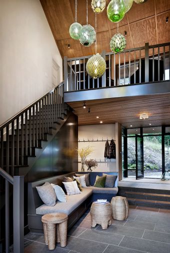Mudroom entry features chandelier with 12 vintage glass floats lighting the painted staircase. Rustic plywood ceiling upstairs contrasts with refined lower. Custom banquette has steel magnetic message board above. Black Tusk Basalt flooring inside and out.