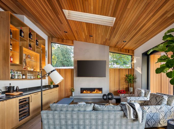 The fireplace brings warmth to living area beneath water-based stained cedar ceiling. Custom white oak liquor cabinet by Warm Tones Woodworking. Interior design by Joelle Jarvis. Wine cooler Eastbank Contractor Appliances.