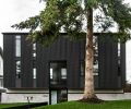 The home’s corrugated metal exterior creates its architectural splendor. Window above entry features perforated metal screen reiterating interior staircase design. Entry walkway adds unexpected diagonal angle to save existing tree’s roots. Evergreen tree provides year-round privacy.