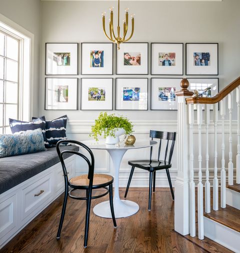 Lawton transformed the area behind staircase by adding a built-in bench, upholstering it with Perennials fabric. Custom wainscoting by Lawton. Six-arm brass Visual Comfort chandelier crowns Pottery Barn frame collection.
