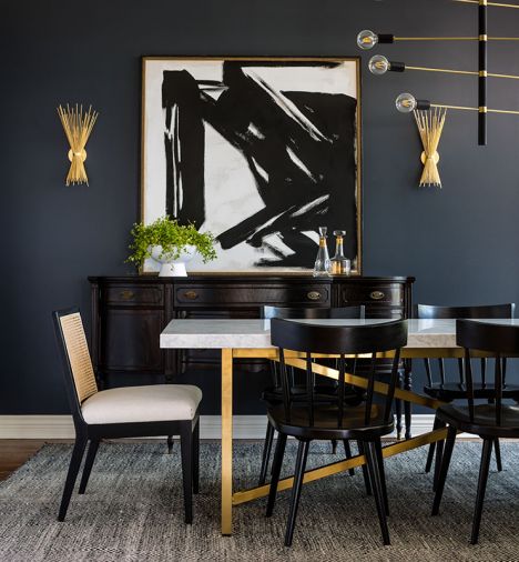 Dramatic dining room transformation includes bold artwork from J Garner Home set against Cyberspace Sherwin Williams walls and Visual Comfort Lighting gilt gold sconces. Dining room showcases gilt gold Visual Comfort sconces. and matte black and brass Hudson Valley Lighting chandelier. Four Hands J Garner Home chairs pair with Restoration Hardware table.