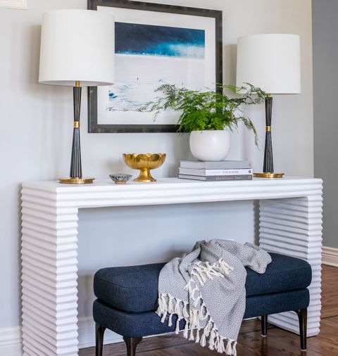 Mr. Brown concrete console table adds graphic appeal to staircase wall. Lawton creates “flex” furniture opportunities with another West Elm bench easy to pull into living area. Pair of console lamps echo brass accents found elsewhere.