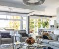 RH Crystal Halo chandelier brightens RH Keane stainless steel and glass square coffee table below. Moon reveals blackened steel moment structural frame separating kitchen from formal dining area. Box beamed dining room ceiling element continues the visual delineation.