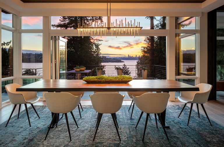 Sentient handcrafted live edge dining table from Brooklyn, New York, art studio glows beneath Cityscape Hubbardton Forge chandelier reiterating Seattle skyline beyond. Sierra Pacific accordion door.