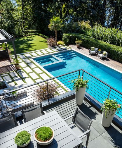 Seen from the second-floor deck seating area with individually precast concrete pavers and custom steel railings, the newly resurfaced pool features new, gradual stepped down entrance alongside spa that gleams in the sunlight. RH Marbella and Aegean outdoor furnishings. Privacy hedge runs length of pool backed by higher shrubs. Retractable canvas roof to capture pine needles protects cabana. Artificial turf looks anything but, with variegated colored blades of “grass.” Turf surrounding individual pavers creates a Greek Key motif.