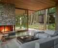 The corner of the living room opens to the Ipe deck and lush forest, and the Western Red Cedar ceilings extend outside. A sectional from Focus One Home and a Toro Lounge Chair by Blu-Dot are cozy spots by the Huckleberry basalt stone fireplace.