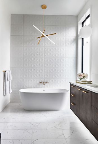Pental 3D Wall geometric tile crowned by West Elm pendant and Delta faucet. Sculptural, free-standing Signature tub adds peace. Vanity cabinets by Hayes Cabinets. Vallelunga Carrara flooring.