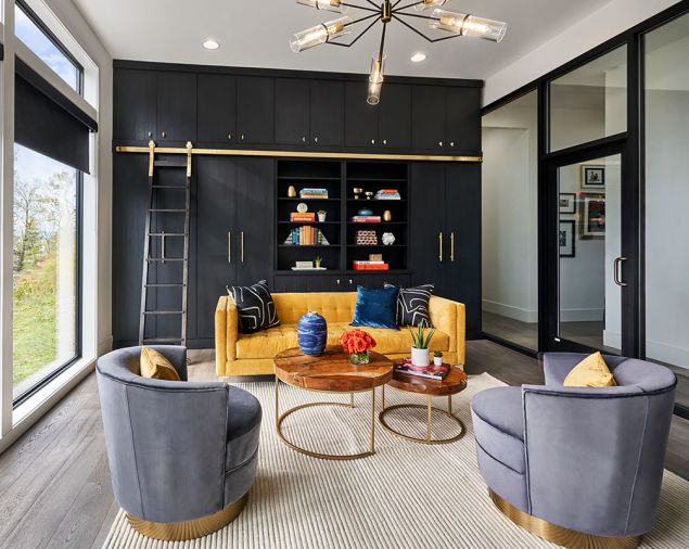 MacLeod-designed library cabinetry trimmed in brass plays off unique chandelier with stunning geometric lines by Troy Lighting Raef Chandelier. Homeowners found colorful floor model sofa and brought it home in their van. Loloi rug grounds scene.