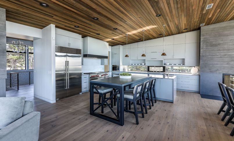 Chris wanted a Mid-Century butterfly style roof seen here where Schouten introduced counter-high horizontal windows he calls “more mural than backsplash.” Modern Dreamline cabinets painted with Sherwin Williams, Ellie Gray. O’Brien’s custom designed table with metal legs by Gregory Holt attaches to quartz island countertop, replicating Blandford’s Arizona kitchen that brings guests comfortably to table while chef works. Hudson Valley task lighting. Low-back Vanguard stools with Maxwell striped fabric and faux leather seats by Pacific Hide & Leather. Rusticated board-formed concrete fireplace with strong horizontal design by Cement Elegance atop polished concrete bottom and steel flush hearth. Sub-Zero refrigerator, Wolf range, Vent-a-Hood, and Asko dishwasher from Standard TV & Appliance.