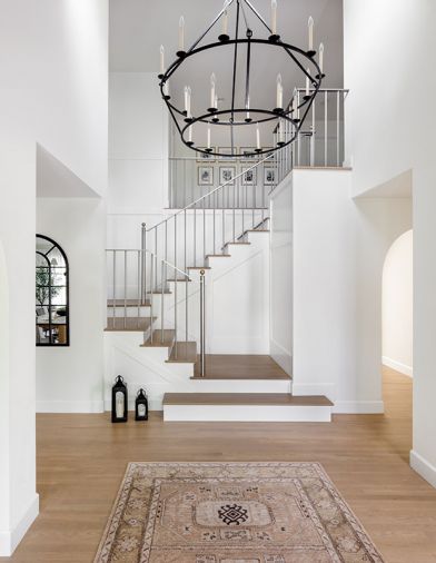 In the entry, a brass and stainless-steel stair railing and oversized chandelier by Visual Comfort are elegant additions.