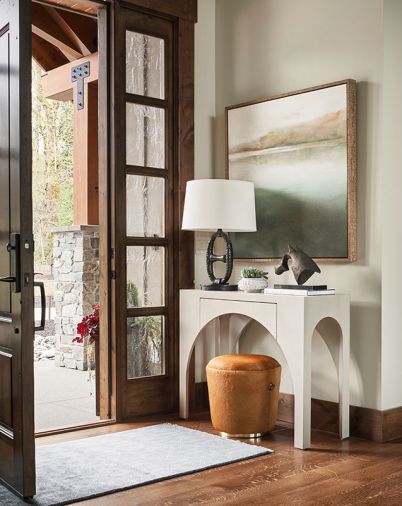 A welcoming guest entry with charcoal and gray wool Surya rug is crowned by Bakers Pond artwork. Console Table in Cliffside Grey teams with warm Arteriors Monroe ottoman.