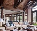 A Parsons square cocktail table in Caramel echoes towering overhead beams. Sea Green accent pillows continue water theme found in Bernhardt Mosaic Side Chai dining chairs. Currey & Co. Broxton Orb bronze dining room chandelier gleams before Sierra Pacific windows.