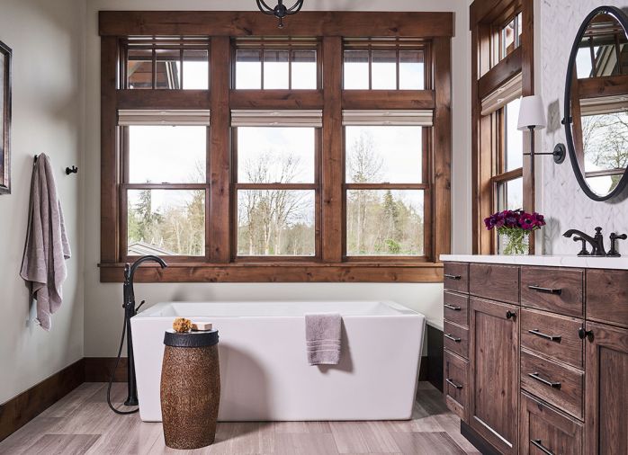 Rustic meets Refined: soft marble mosaic backs double vanity sink wall. Dainty Bryant sconce in bronze finish adds feminine touch to Rustic Hickory cabinets. Tolson Oval Pivot Mirror in oil rubbed bronze from Rejuvenation. Comfy Bianca Collection freestanding bath. Flooring: vein cut honed Chenille White Daltile.