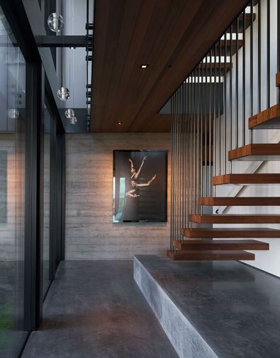 Stacked staircases with walnut treads feature suspended blackened steel rods representing Northwest rain. Limestone and concrete floor with platform aids shoe removal.
