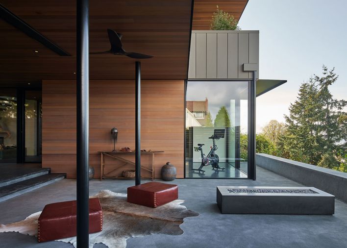 Gym is visible through entry courtyard cooled by Big Ass “Haiku” fan. Pair of red leather poufs by The Citizenry cozy up to Paloform Robata 72 concrete fireplace.