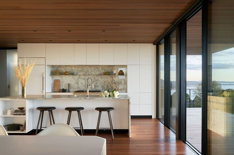 Mater MD Counter Stools in Sirka Gray stained Beech tuck beneath island overhang. Waterfall island countertop echoes range marble backsplash.