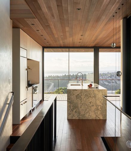 Venetian plaster stairwall on upper floor bridge connects East-facing roof deck and media room to West-facing great room. Island’s waterfall Bianco Treviso marble with Julien J7 sink and Brizo Litze articulating faucet. Bocci pendants. Walnut flooring grounds Western Red Cedar ceiling.