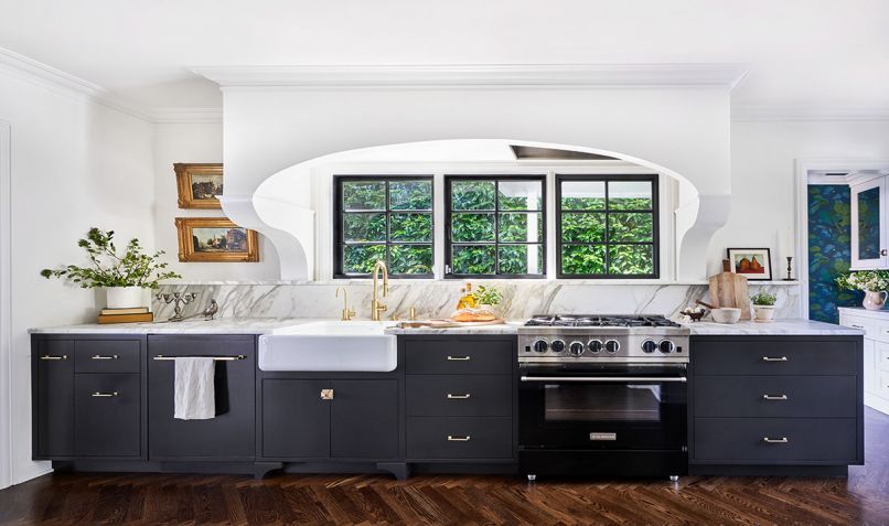 A bank of black cabinets by L&Z Specialties match custom-colored Blue Star range for modern flare. Stunning extra honed Calacatta Daltile installed by Alpha StoneWorks features beautifully crafted 4' linear ledge that draws eye to custom corbels supporting classic arch housing Vent-A-Hood. Rejuvenation Mission unlaquered brass cabinetry hardware is repeated on the more traditional (unseen) white cabinets opposite. Kohler Whitehaven sink from Ferguson. Arlene ditched low-quality cabinets and replaced flipper’s “hideous” wood floors with herringbone oak floors by Champion Hardwoods to better match original floors in adjacent dining room now made more accessible and alluring through a 5' wide opening.