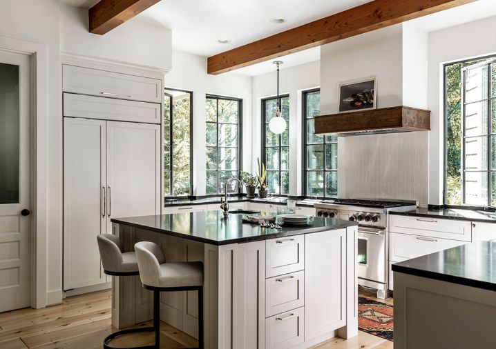 The kitchen features natural elements, including soapstone countertops, solid-wood cabinets, and a custom wood range hood that complements the fireplace’s wooden mantel opposite. Waterstone faucet from Best Plumbing shines when light infuses the space, thanks to the show-stopping new windows. Materials were chosen to evoke memories of the couple’s French countryside travels.