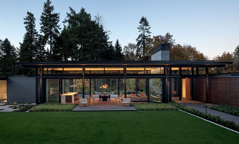 The horizontality of the great room maximizes its sense of serenity. Furnishings by FQ Designs Group were specifically chosen for their simplicity in style and low- to-the-floor-profile to reiterate the architectural design. 2.ink Studio flanks the front terrace with 12' Berkeley Sedge. A mix of ferns and Japanese forest grass left. Lakeside Lumber siding mimics Japanese Shoji screens at entrance. Kolbe VistaLuxe clerestory windows from Portland Millwork rise to roof creating floating roof effect. Fireplace chimney rises out of the roof adding dramatic verticality. Gloster “Kay” low-back rocking chairs with Gloster “Blow” side tables on terrace.