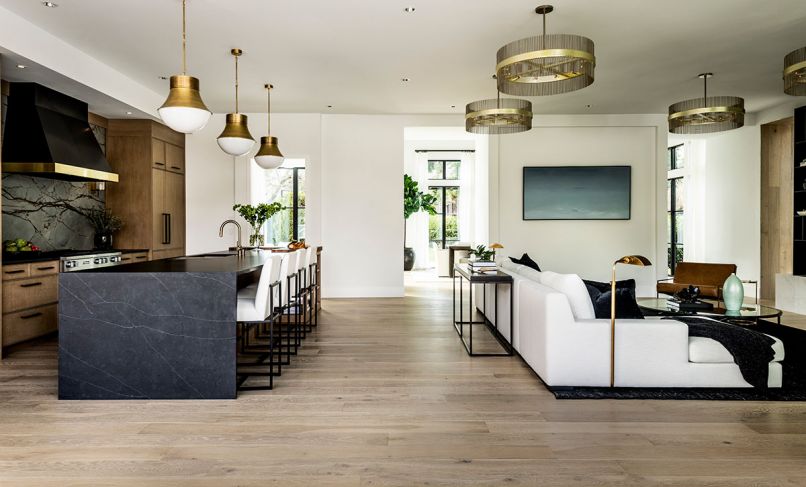 The living room and kitchen sit just beyond the dining room and “Sun Hall.” Furnishings and artwork from Restoration Hardware outfit the seating area, while pale wood cabinets from Signature Custom Cabinetry anchor the kitchen. The floors are oak throughout. “Oak is just really stunning and has so much warmth and character to it, but it’s also very clean,” says interior designer Kowalski. “It’s not overly rustic.”