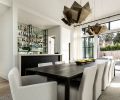 In the dining room, sculptural light fixtures from Curry & Co. are suspended over a table, chairs, and rug from Restoration Hardware. The adjacent bartop is wrapped with a porcelain slab serving counter from CR Floors. The exterior glass double doors open to a sun patio at the front of the home.