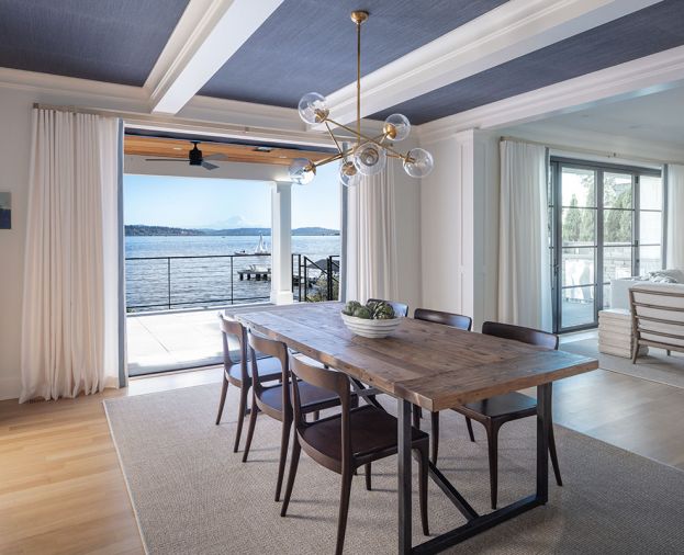 The home has all new millwork, such as the coffered ceiling in the dining room. Stroud placed Phillip Jeffries Grasscloth between the beams. Ten-foot-wide LaCantina Doors open to the view, and are framed in custom curtains made from Pindler & Pindler linen fabric. A Restoration Hardware table is surrounded by Redford House chairs and lit by a Visual Comfort chandelier. The rug is DMI.