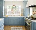 Above the new sink, large windows overlook the backyard and provide an easy pass-through to a small outdoor kitchen area. Ray creates visual calm in the small space by encasing large appliances. Here a Sub-Zero freezer to the left of the sink is camouflaged and then balanced by the taller storage cabinet on the right.