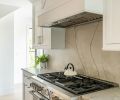 White Santorini quartzite range backsplash mirrors countertops from Noble Interiors & Design. Classic Brass hardware from Builders Hardware. Thermador range.