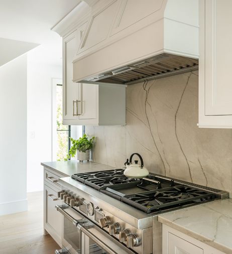 White Santorini quartzite range backsplash mirrors countertops from Noble Interiors & Design. Classic Brass hardware from Builders Hardware. Thermador range.