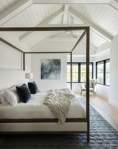 Black Restoration Hardware metal four-poster reiterates Pella window frames set against Chantilly Lace Benjamin Moore walls. Camelion Design custom chair. Commissioned painting draws eye upward to vaulted ceiling, its blue tones echoing Loloi area rug and accent bed pillows.