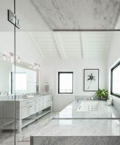 Seen from the shower, primary bath features vaulted ceiling and Jacuzzi tub with natural Carrera marble deck and counter by Noble Interiors & Design. Amish built double vanity with Water Street Hardware from Builders Hardware. Restoration Hardware vanity lighting.