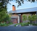 Existing agricultural buildings inspired architect Kirsten Ring Murray to create a steeply pitched metal roof. Horizontal torched spruce siding resembles weathered barnwood. Steel pivot entry door plays off utility room at left, its patina changing with exposure to elements. Island Gardens Company landscaping features a trio of willows creating symmetry with tree at left. Small evergreen Douglas Iris, heather, and creeping thyme are ground cover. Deer fence posts are small steel I-beams.