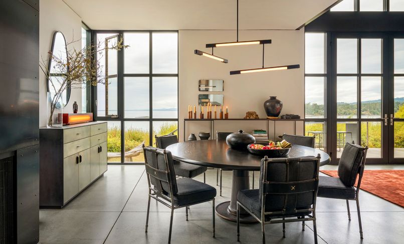 A Wintercheck Factory light sits atop a credenza by WÜD Furniture, crowned by a Brian Paquette mirror. Custom dining chairs by Mexican craftsman at Casamidy. Troscan Design dining table. Mary Wallis matte black three-tiered light fixture. Corner casement Fleetwood window provides cross breeze. Poured and ground in place concrete floors with light green tint feature radiant heat. “We used a floor grinder and polisher to give it a unique finish,” says Lowe.