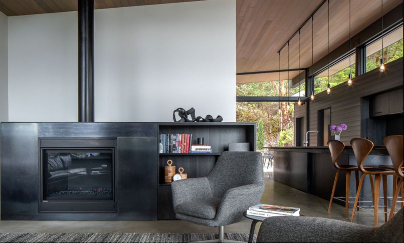 In the living room, chairs from Kasala sit in front of a Montigo HL38 linear burner fireplace. The kitchen includes hardware and oak cabinets stained black, both by Space Theory, and Bosch kitchen appliances. The wood ceilings are clear cedar engineered tongue-and-groove, a product called “Dolly Varden” by Shaker Town.