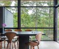 Marvin windows frame views of all aspects of the site, from water to forest. The kitchen island is topped in Absolute Black granite in a silk finish, with counter-height Cherner stools beneath. The pendant lights above are suspended from a track, both by Bruck Lighting.