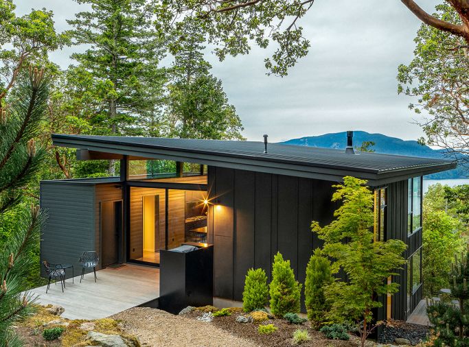 The exterior is covered in T1-11 plywood with randomly spaced battens, and the roof is standing seam metal. The exterior storage, enclosed entry, and interior pantry walls are all wrapped in the same material for continuity from inside to out.