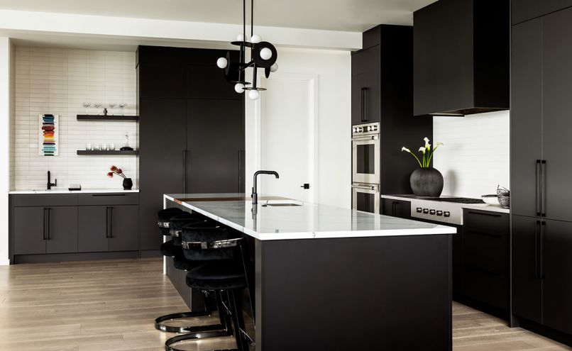 Clean lines and loft-inspired colors and fixtures ground and define the kitchen in what otherwise might have felt like a cavernous space. Contemporary lighting from Kelly Wearstler’s architectural Nodes line is used throughout the home, including a statement chandelier over the kitchen island. Glossa and Kestenbaum’s skill with space planning resulted in high-functioning spaces for enthusiastic home cooks and entertainers. Sleek cabinetry frame Wolf appliances and a concealed Vent-A-Hood. The oversized island features a built-in walnut cutting board from Cross Cut Woodworks and a dramatic waterfall countertop of PentalQuartz.