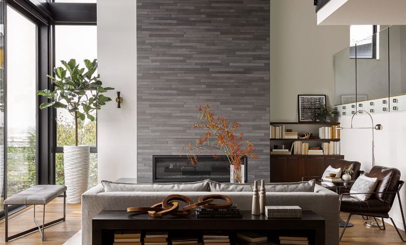 White Space Design Group anchors darker palette as a backdrop that allows view to shine - including the MOSA fireplace tile that features three different tones in a single colorway. Restoration Hardware floor lamp right lights a pair of Pottery Barn Owen Leather Armchairs. The Adams’ handblown glass plates by Czech SkLO adorn wall between the living room and Williams’ den tucked at right behind a glass wall that opens onto water view.