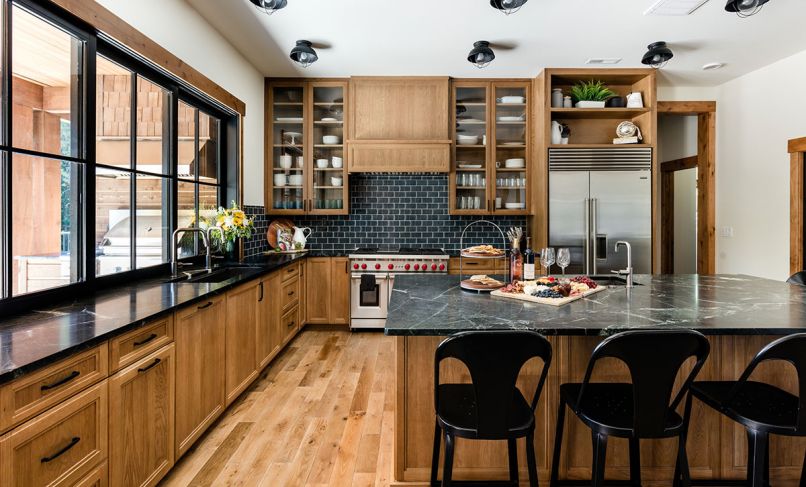 In the kitchen, the rift white oak cabinetry has a custom-designed door style and integrated LED lighting, all fabricated by Northwest Custom Interiors. The “Sage Soapstone” countertops are a lovely contrast to the wood tones, and sync with the Walker Zanger tile on the backsplash. “Sebring” sconces from Sea Gull Lighting at the ceiling and Pottery Barn stools tucked under the counter lend an industrial flair.