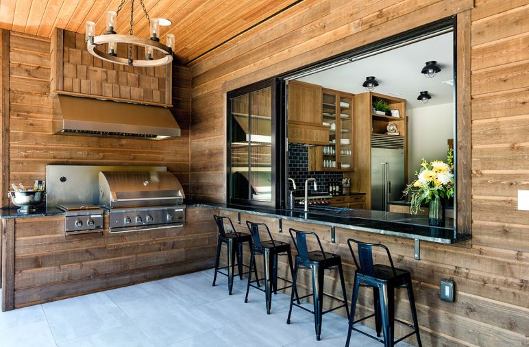 A chandelier from Shades of Light illuminates the outdoor grill station, accessed by a pass-through window from the kitchen.