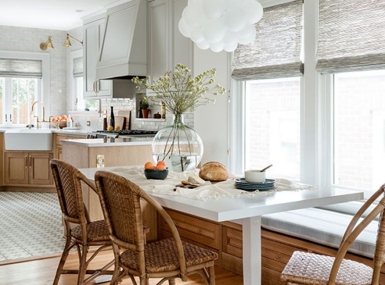 Custom banquette by Superior Cabinets features Thibaut fabric from The Dixon Group. Benjamin Moore Snowfall White walls with Balboa Mist millwork echo painted upper kitchen cabinets. Bistro style Pottery Barn chairs grace white painted Gat Creek (Designer Furniture Galleries) dining table. The Light Factory fixture provides touch of whimsy.