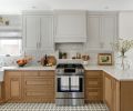 The kitchen is grounded by Cement Tile Shop flooring featuring a bold blue star pattern reminiscent of European bistros the couple had visited while abroad. Above, Superior Cabinets custom wood lower cabinets pair with uppers painted in Hidden Cove gray. Between the two, texture sparkles amidst the Clé Tile backsplash with recessed niche. Tucked beneath the Vent-A-Hood, the recessed niche keeps cooking oils off counter. Brass jewel-toned adornments include Fox Mill lighting and Rohl fixtures from Ferguson, the supplier of all Bosch appliances - range, dishwasher, and refrigerator. After informative trips to local slab stores, Erika chose easy-to-clean Cambria quartz countertops.