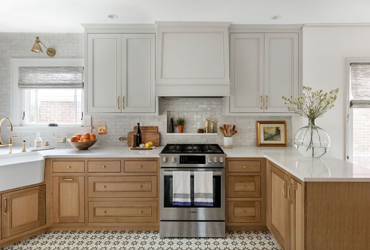 The kitchen is grounded by Cement Tile Shop flooring featuring a bold blue star pattern reminiscent of European bistros the couple had visited while abroad. Above, Superior Cabinets custom wood lower cabinets pair with uppers painted in Hidden Cove gray. Between the two, texture sparkles amidst the Clé Tile backsplash with recessed niche. Tucked beneath the Vent-A-Hood, the recessed niche keeps cooking oils off counter. Brass jewel-toned adornments include Fox Mill lighting and Rohl fixtures from Ferguson, the supplier of all Bosch appliances - range, dishwasher, and refrigerator. After informative trips to local slab stores, Erika chose easy-to-clean Cambria quartz countertops.
