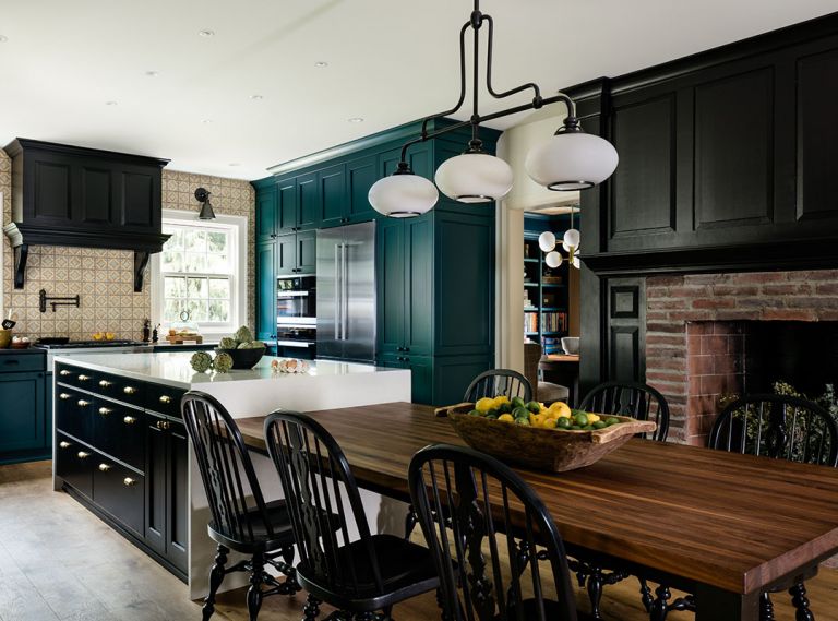 In the kitchen, cabinets by United Wholesale are painted a vibrant teal, and grounded with black accents, via the black pearl granite counters, Hudson Valley Lighting, stove hood, and fireplace surround. Rowland carried the patterned Ann Sacks tile to the ceiling, and specified reclaimed wood shelves to suspend over the windows, so everyday items are easily accessed. A large island covered in Upper Spectrum Maple White quartz cedes into a comfortable, custom seating area in front of the fireplace. Mafi wood flooring by Greenhome Solutions brings character.